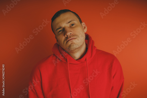 Crazy and charismatic guy posing on an orange background. A man in a red tracksuit. © Anton Dios