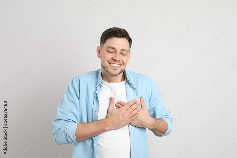 Portrait of man holding hands near heart on light background Portrait of man holding hands near heart on light background
