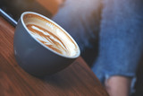 Closeup image of a blue cup of hot latte coffee on wooden table with woman sitting in cafe