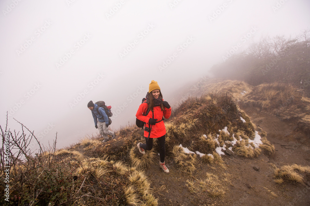 Obraz premium Hikers couple with backpacks walking on top of mountain in fog above clouds