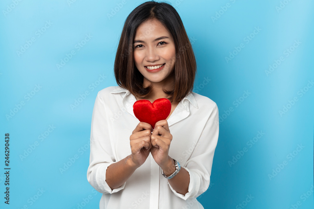 Love and valentines day, asian girl holding red heart shape isolated on blue background Love and valentines day, asian girl holding red heart shape isolated on blue background