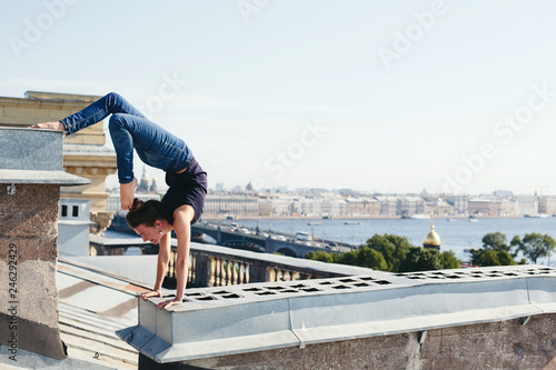 Young female doing yoga, standing on her hands on roof top in city center
