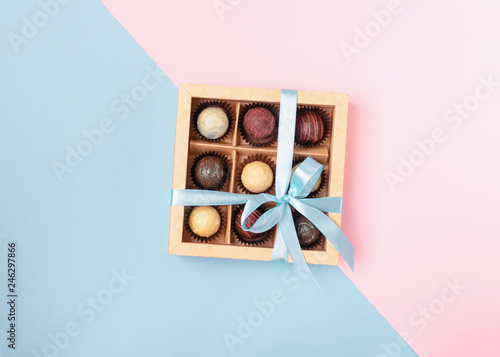 Various chocolates in crafting paper box with a satin blue ribbon on a brightly colored background. Flat lay concept.