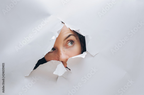 A girl with a cunning expression. Portrait of a woman looking through the hole in white paper. Distrustful look. Women's curiosity and gossip. A jealous wife. photo