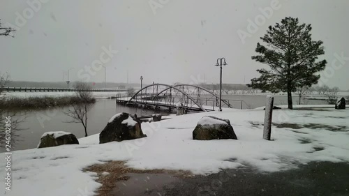 Watching the snow fall in slow motion on small Texas city lake with beautiful walking bridge, trees, lake, rocks and gray skies. photo