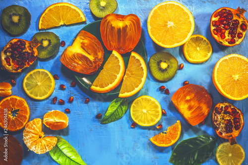 Fototapeta Naklejka Na Ścianę i Meble -  sliced ​​citrus fruits on a blue painted board. orange, kiwi, pomegranate, persimmon, mandarin.