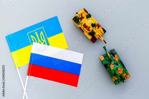 War, confrontation concept. Russia, Ukraine. Tanks toy near russian and Ukrainianflag on grey background top view photo