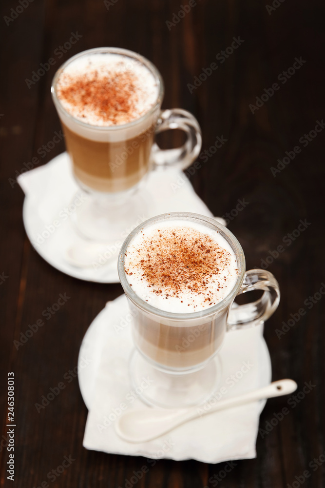 Coffee in glass on the wooden background. A glass with cappuccino and cinnamon. Coffee in glass on the wooden background. A glass with cappuccino and cinnamon.