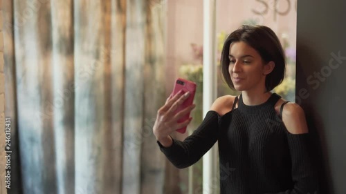 Beautiful girl is standing near the showcase in a flower shop and talking on the phone in a video chat. Girl has very expressive face features and movements. photo