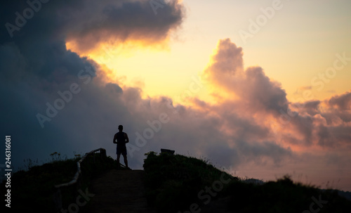 man stands on a hill against the sky at sunset