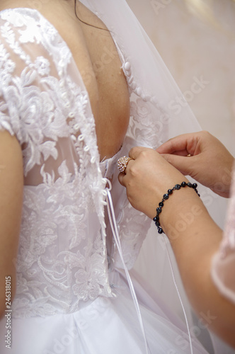 Woman laces up corset on bride's  waist. Morning bride concept