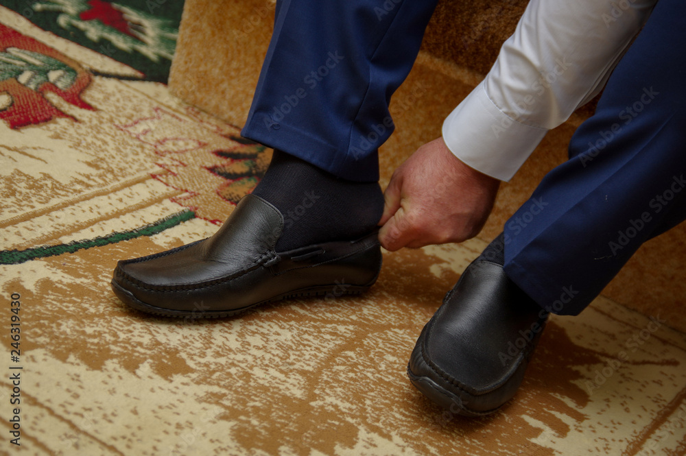 The man ties the shoelaces on the shoes. Business formal style of clothing. Official event. Wedding. Morning of the groom. Cropped image The man ties the shoelaces on the shoes. Business formal style of clothing. Official event. Wedding. Morning of the groom. Cropped image