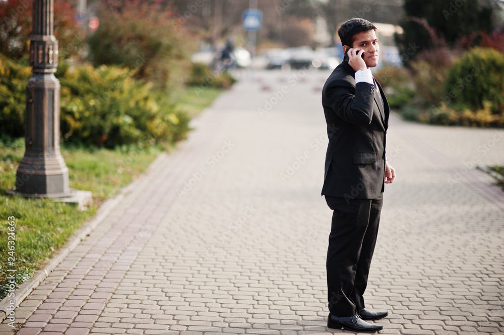 Elegant south asian indian business man in black suit speaking at mobile phone.