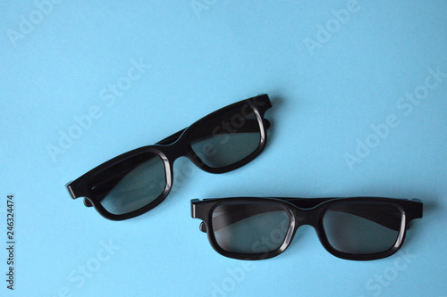Two black plastic glasses on a blue background. Sunglasses, 3D glasses for the cinema.