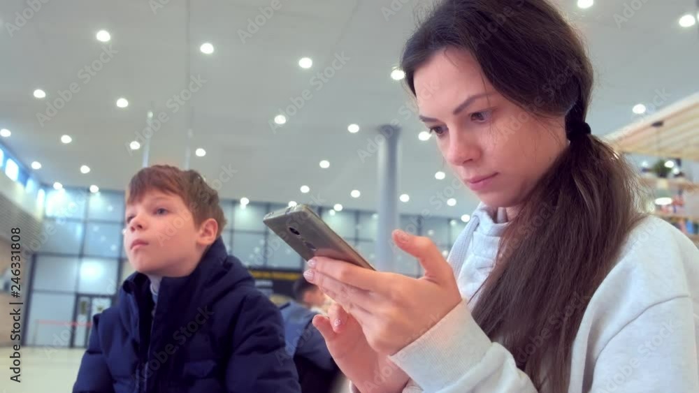 Woman with her son check-in online registration on her mobile phone in airport hall. Woman with her son check-in online registration on her mobile phone in airport hall.