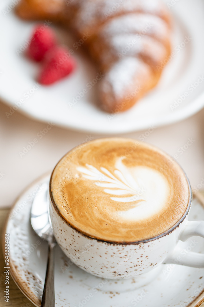 Coffee cappuccino with croissant on white plate in restaurant. Light morning Breakfast, fresh warm pastries and raspberries Coffee cappuccino with croissant on white plate in restaurant. Light morning Breakfast, fresh warm pastries and raspberries