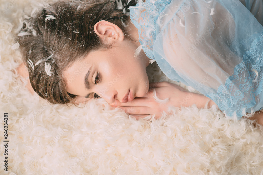 Soft and caring mattress. Young woman in sleep wear. Cute girl relaxing on feather bed pillow and mattress. Pretty girl in silky pajamas with feather in long hair. Wearing pajamas to sleep well Soft and caring mattress. Young woman in sleep wear. Cute girl relaxing on feather bed pillow and mattress. Pretty girl in silky pajamas with feather in long hair. Wearing pajamas to sleep well