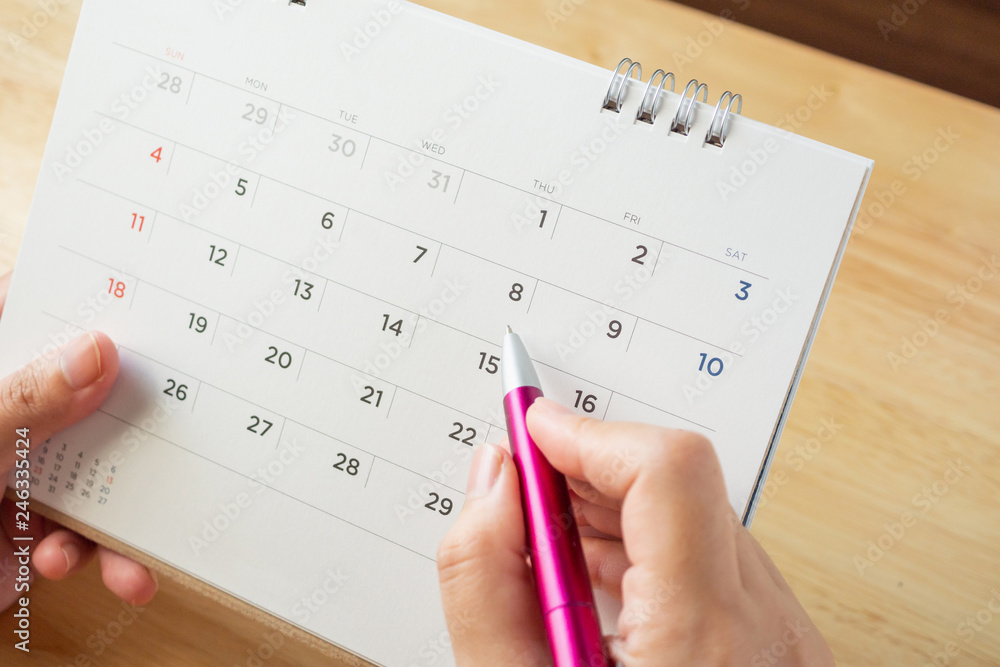 calendar page with female hand holding pen on desk table calendar page with female hand holding pen on desk table