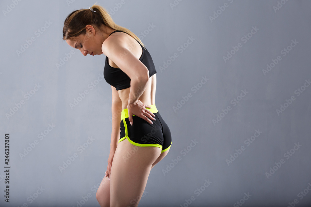 Beautiful female athlete in a sport suit touches a sore back. Concept of  protecting the waist from sprains and bruises Stock Photo