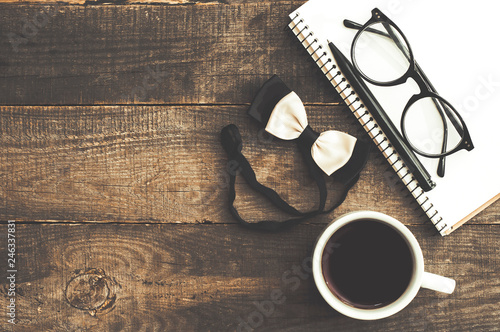 Cup of coffee, bow tie, notebook, glasses and pen on wooden background. Top view
