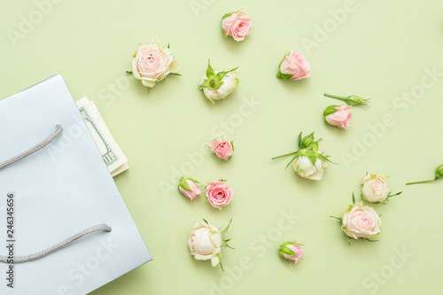 Birthday celebration concept. Fresh roses on green background. Gift bag with money. Flat lay.