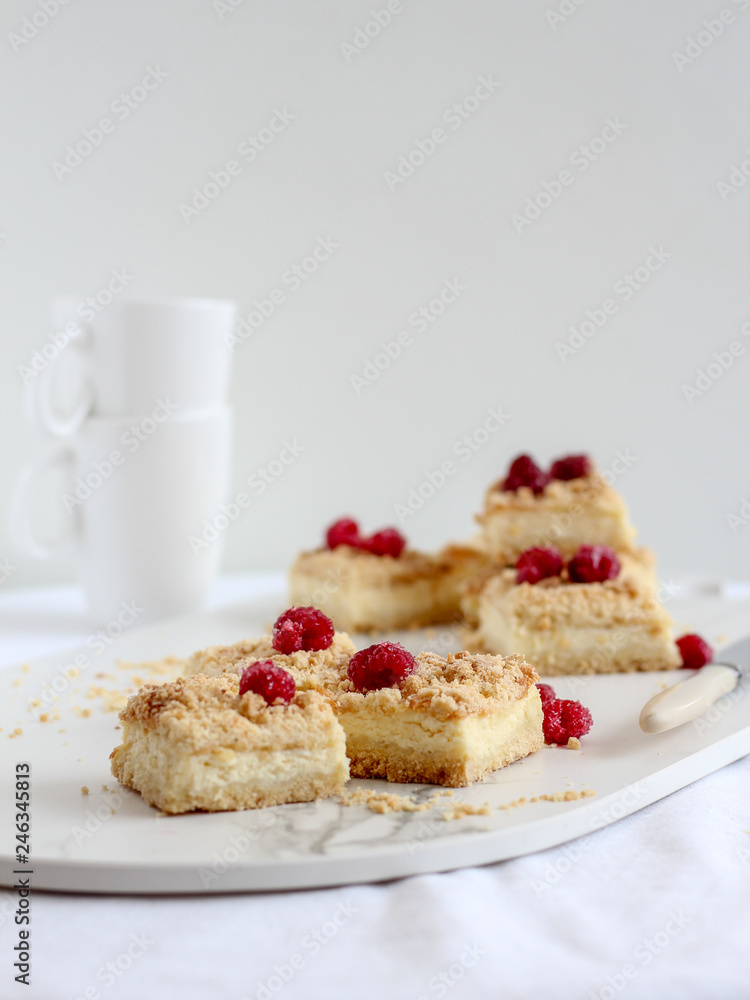 Sliced crumble pie with raspberries on top on a marble plate and cups in the background Sliced crumble pie with raspberries on top on a marble plate and cups in the background