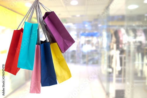 Crop female hand holding colorful paper bags on background of shopping center.