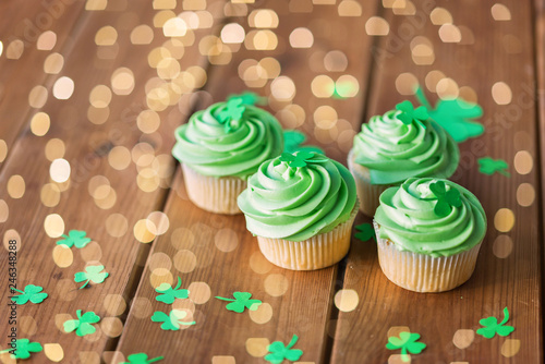 st patricks day  food and holidays concept - green cupcakes and shamrock on wooden table