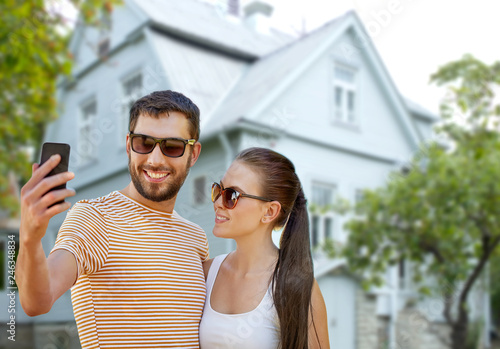technology and people concept - happy couple taking selfie by smartphone in summer over house background © Syda Productions