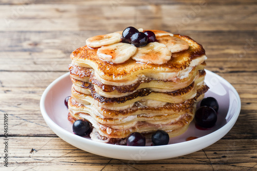 Pancake cake with bananas and berry syrup, selective focus, dark background.