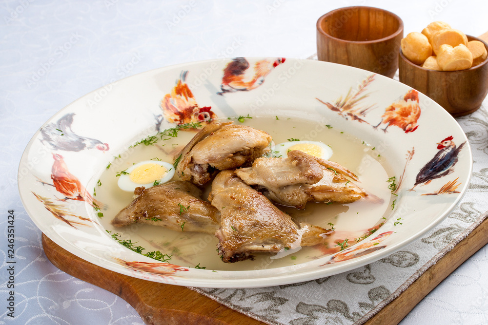 Quail broth with crackers and herbs on a wooden board. On white background.