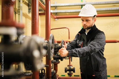 worker with protective helmet turns valve on industrial refinery oil pipes.