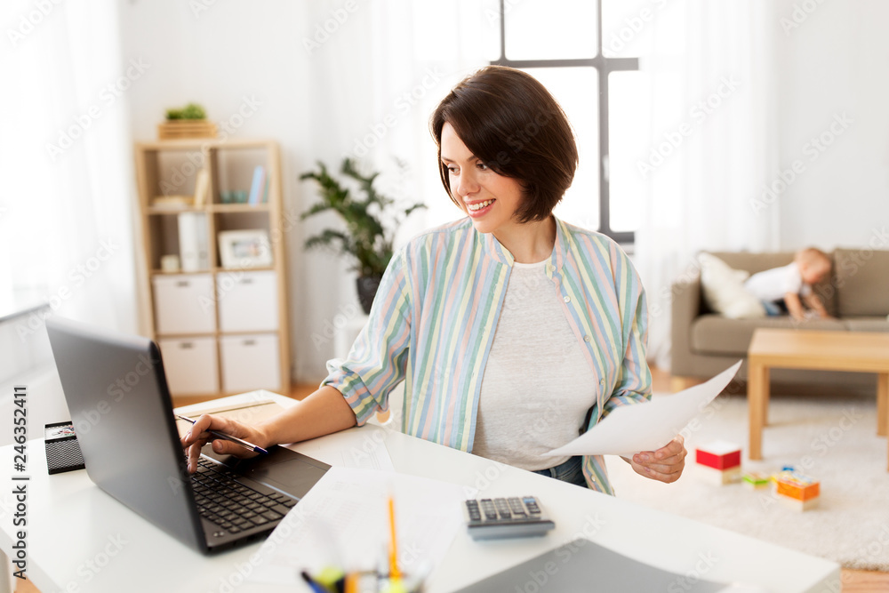 multi-tasking, freelance and motherhood concept - mother working with papers at laptop computer and baby boy at home office multi-tasking, freelance and motherhood concept - mother working with papers at laptop computer and baby boy at home office