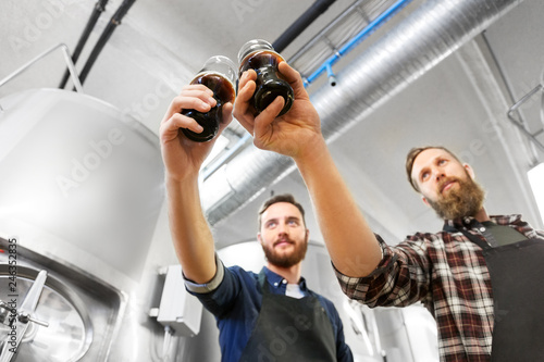 alcohol production, manufacture, business and people concept - male brewers clinking glasses of craft beer at brewery