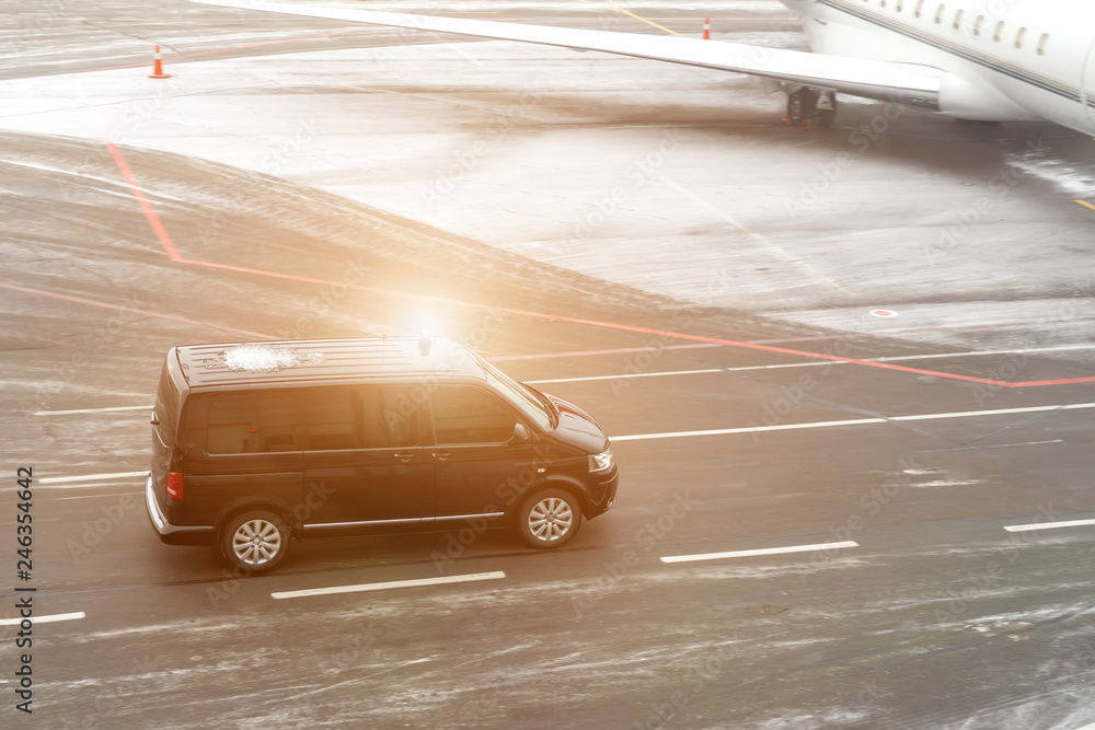 Φωτογραφία Black VIP service van running on airport taxiway with blurred private jet on background