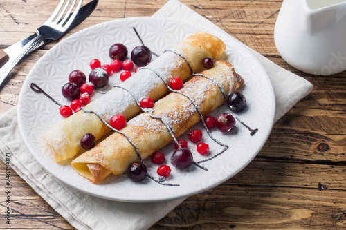 Pancakes tube with chocolate and berries on a plate. Wooden background.