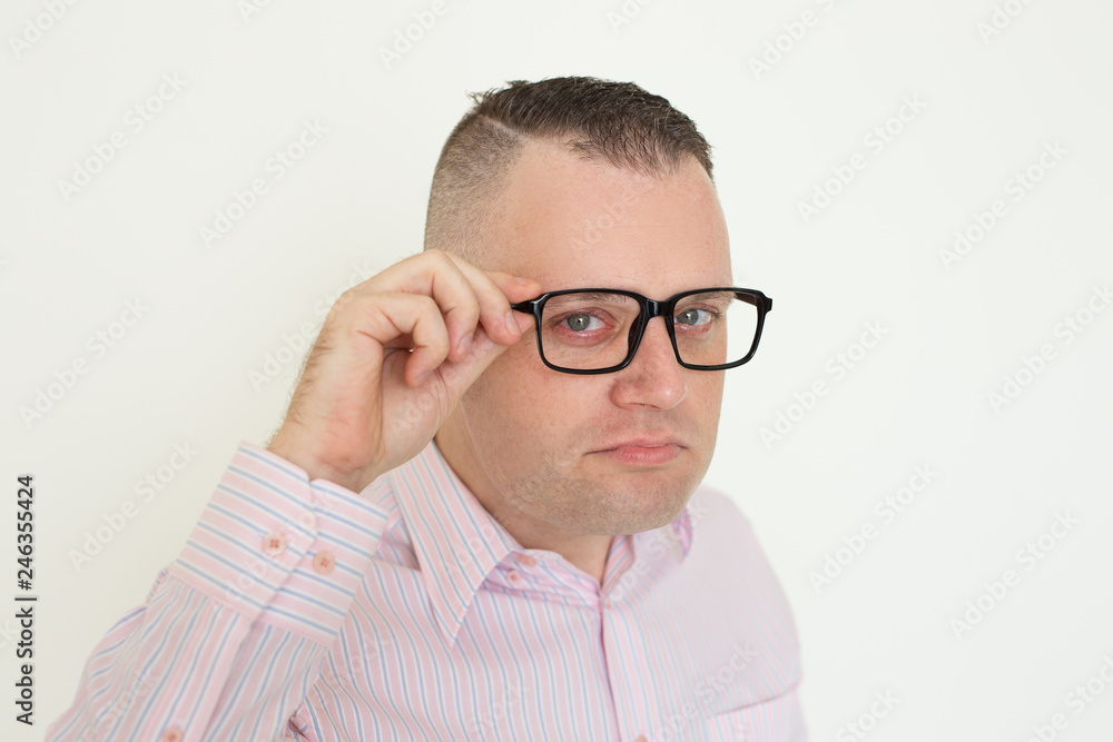 Serious suspicious office employee touching temple of eyeglasses. Closeup of young Caucasian man adjusting glasses and looking at camera. Glasses wearing concept Serious suspicious office employee touching temple of eyeglasses. Closeup of young Caucasian man adjusting glasses and looking at camera. Glasses wearing concept