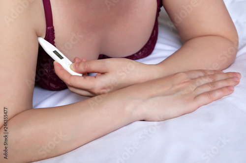 Woman measures body temperature under his arm with digital thermometer. Girl in sexy bra lying in the bed  concept of cold and flu  fever  illness