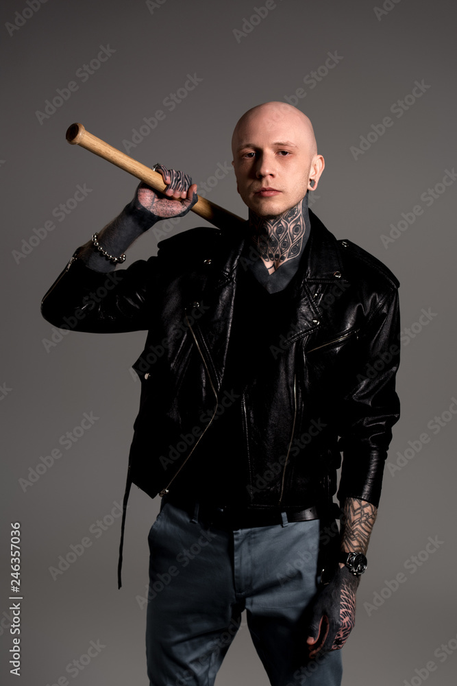 bald tattooed man in leather jacket holding baseball bat and looking at camera isolated on grey bald tattooed man in leather jacket holding baseball bat and looking at camera isolated on grey