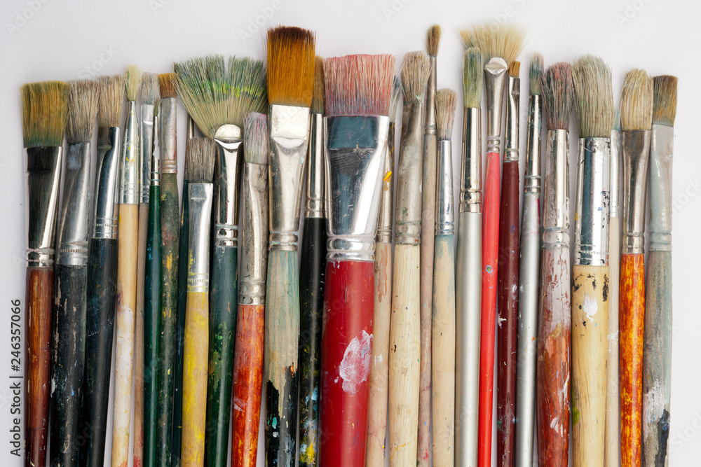 Fototapeta premium A collection of well used art paint brushes on white paper surface