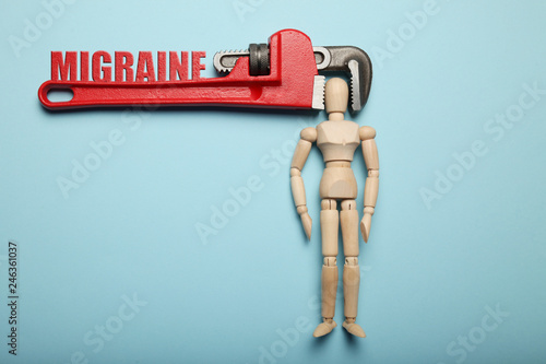 Wooden figure of man with his head clamped in vice with inscription migraine. Pain, stress, headache. photo