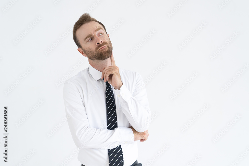 Pensive handsome young businessman looking aside. Frowning introspective man with beard contemplating while holding finger on chin. Planning concept Pensive handsome young businessman looking aside. Frowning introspective man with beard contemplating while holding finger on chin. Planning concept