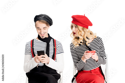 french woman in beret looking at man using smartphone while sitting on chair isolated on white