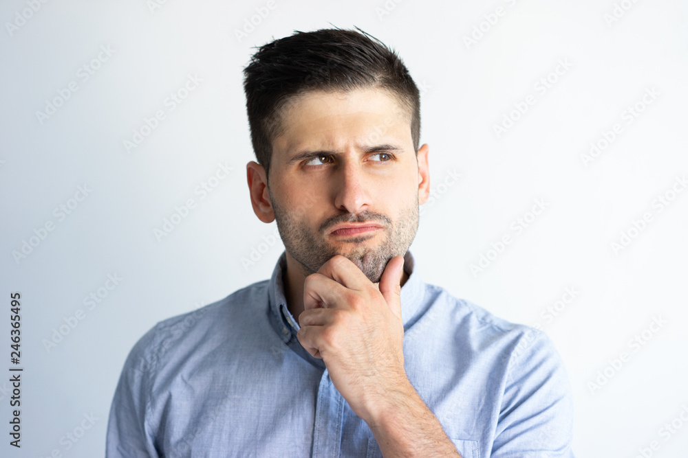 Pensive frowning guy in casual making decision. Young Caucasian man with stubble touching and scratching chin and staring into vacancy. Thinking concept Pensive frowning guy in casual making decision. Young Caucasian man with stubble touching and scratching chin and staring into vacancy. Thinking concept