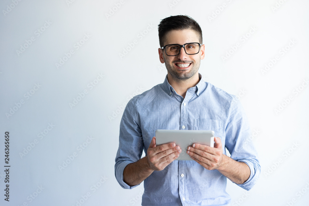 Portrait of cheerful excited tablet user wearing eyeglasses. Young Caucasian man in casual holding tablet and smiling at camera. Mobile internet concept Portrait of cheerful excited tablet user wearing eyeglasses. Young Caucasian man in casual holding tablet and smiling at camera. Mobile internet concept