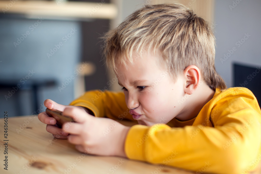 Children, technology and internet concept. Little smiling boy playing games on digital smartphone Children, technology and internet concept. Little smiling boy playing games on digital smartphone