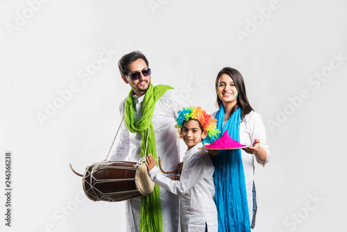 Indian young couple with kid celebrating holi festival. Dancing and playing drums and holding plate full of colours photo