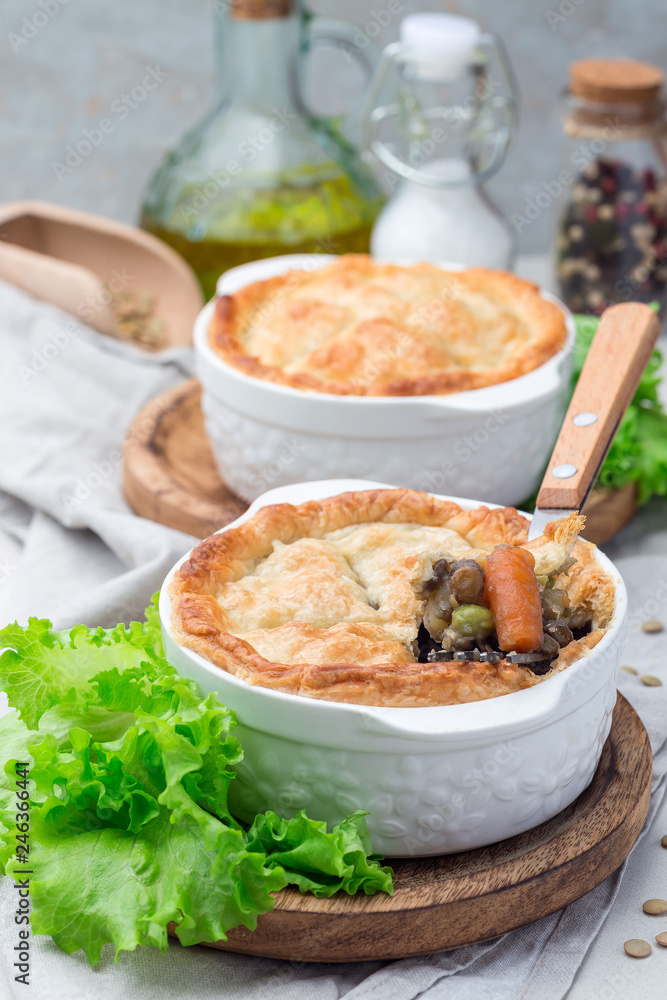 Vegetarian pot pie with lentil, mushroom, potato, carrot and green peas, covered with puff pastry, in a baking dish, vertical