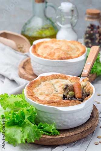 Vegetarian pot pie with lentil, mushroom, potato, carrot and green peas, covered with puff pastry, in a baking dish, vertical