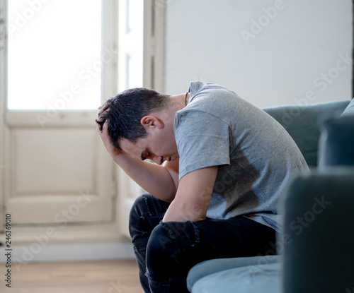 Young man suffering from depression lying on sofa alone at home feeling frustrated and hopeless